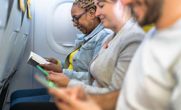 Passengers reading book and using mobile smartphones during airplane trip