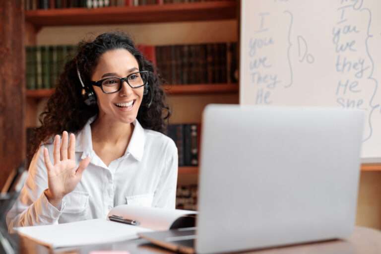 Digital nomad sitting at desk, using computer and waving to webcam